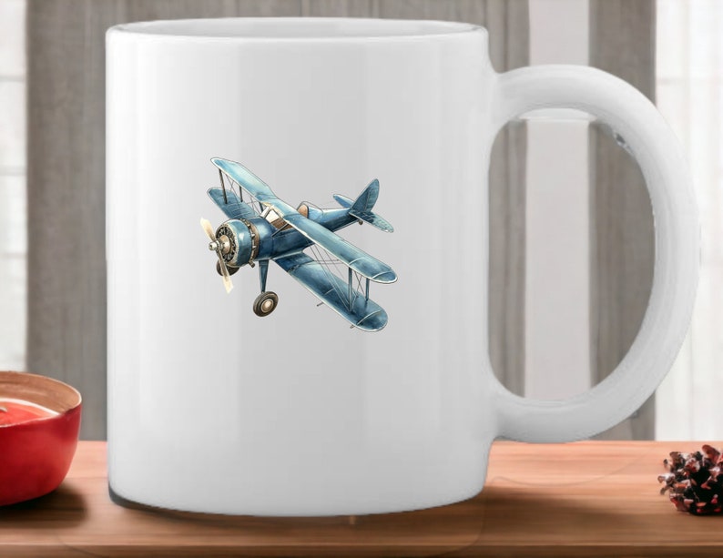 Op de afbeelding: Witte keramische mok met een illustratie van een blauw en wit vintage vliegtuig.