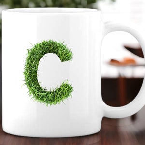May include: White ceramic mug with a green grass letter C design.