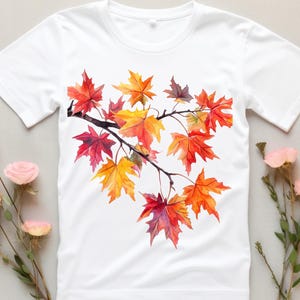 K&ouml;nnte beinhalten: Wei&szlig;es T-Shirt mit einem Aquarell-Design eines Zweigs mit Herbstbl&auml;ttern in Rot-, Orange- und Gelbt&ouml;nen.