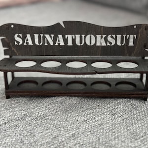 May include: A wooden stand with the text "SAUNATUOKSUT" on the top. The stand has two shelves with six round holes on each shelf.
