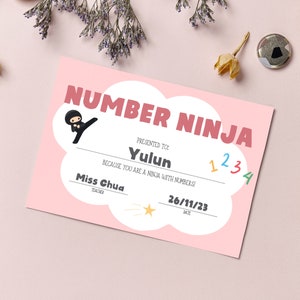 May include: A pink certificate with a cloud shape, reading "NUMBER NINJA" in red letters. It says "Presented to Yulun because you are a ninja with numbers!" and is signed by "Miss Chua, Teacher" with the date "26/11/23".