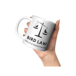 May include: White ceramic mug with a black and white logo that says "Bird Law Kelly & Associates". The logo features a scale with two birds on it.