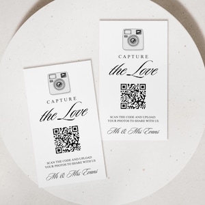 May include: Two white cards with the text "CAPTURE the Love" and a camera icon. Each card has a QR code and the text "SCAN THE CODE AND UPLOAD YOUR PHOTOS TO SHARE WITH US Mr & Mrs Evans."