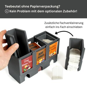 Op de afbeelding: Een donkergrijze theezakjes-organizer van kunststof met meerdere vakken. De unit is voorzien van uitneembare verdelers om de ruimte aan te passen. Theezakjes zijn zichtbaar in de vakken, inclusief labels zoals Cozy Winter Tea, Bear Power en Rooibos & Vanilla.
