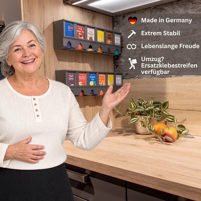 Op de afbeelding: Twee donkergrijze wand-theezakjesdispensers met meerdere vakken, elk met diverse kleurrijke theedoosjes. De eenheden bevatten de tekst Made in Germany, Extrem Stabil, Lebenslange Freude en Umzug? Ersatzklebestreifen verf&uuml;gbar.