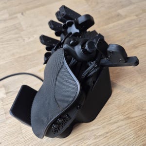 Könnte beinhalten: Ein schwarzer VR-Controller mit mehreren Finger-Tracking-Sensoren und einem strukturierten Griff. Der Controller hat einen Joystick, Tasten und eine Handschlaufe. Das Wort "CYBORG" ist auf der Seite des Controllers sichtbar.