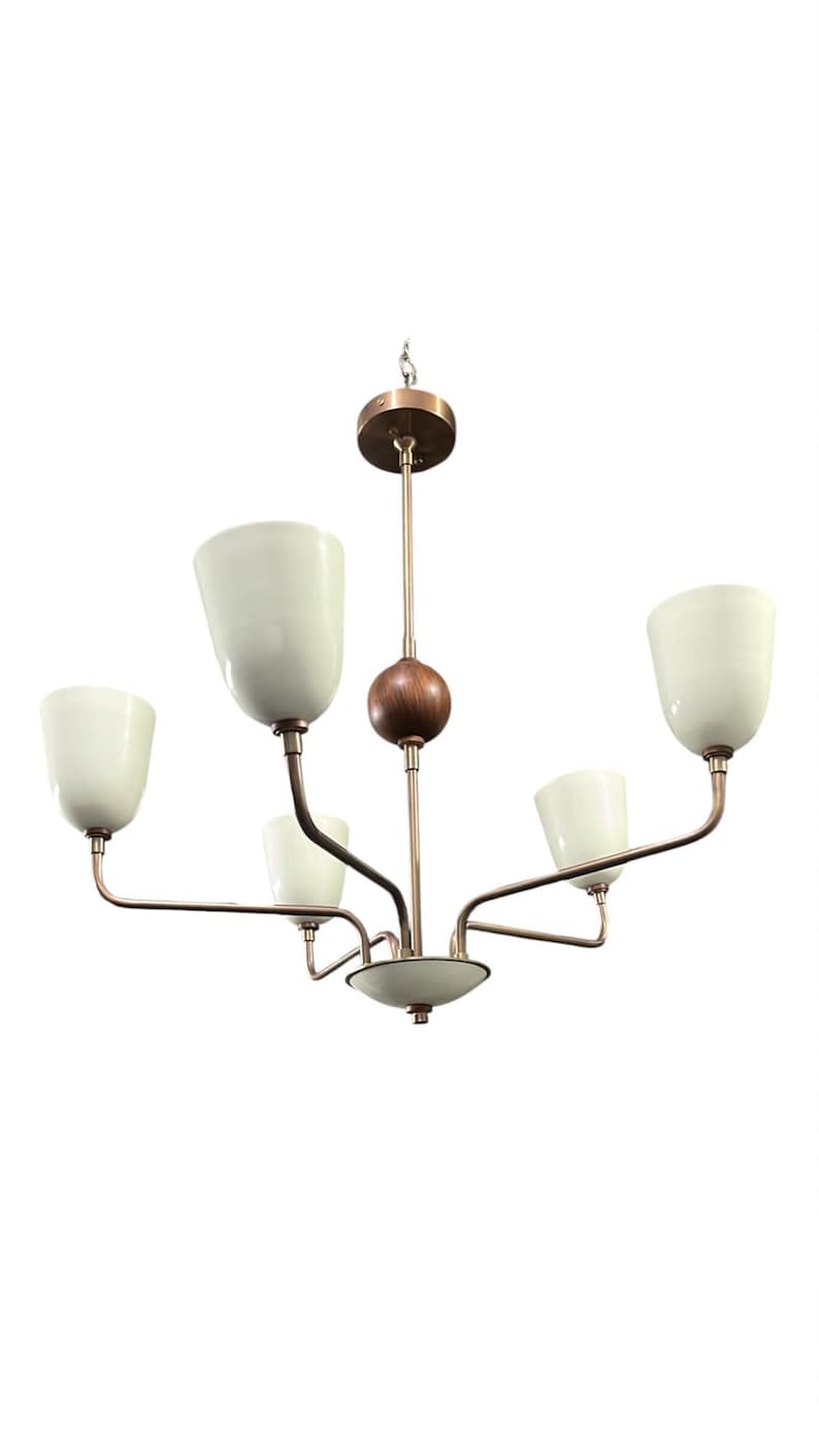 Puede incluir: Un candelabro de estilo retro con cinco pantallas de vidrio blanco roto. La l&aacute;mpara tiene un acabado bronce con un detalle esf&eacute;rico de madera. Los brazos se extienden desde un punto central, creando un dise&ntilde;o equilibrado.