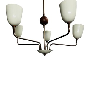 Puede incluir: Un candelabro de estilo vintage con cinco pantallas de vidrio blanco en forma de tulip&aacute;n. La l&aacute;mpara tiene un acabado de bronce con un elemento de madera oscura. Los brazos se extienden desde un punto central, creando un dise&ntilde;o equilibrado y elegante.