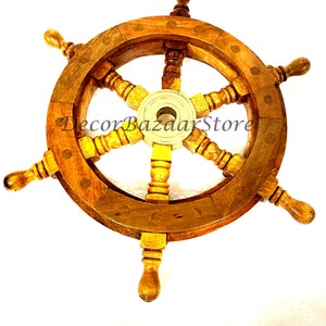 May include: A wooden ship's wheel with brass accents and six spokes. The wheel is brown with a light wood grain and has a brass center hub. The wheel is mounted on a white background.
