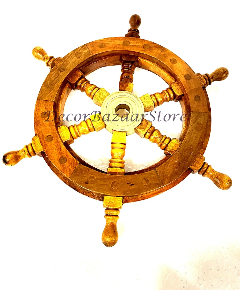 May include: A wooden ship's wheel with brass accents and six spokes. The wheel is brown with a light wood grain and has a brass center hub. The wheel is mounted on a white background.