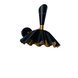 Op de afbeelding: Een zwart en goudkleurige wandlamp met een uniek ontwerp. De lamp heeft een zwarte, kegelvormige top met kleine decoratieve gaatjes. De kap is donkergroen met een gerimpelde rand en een gouden binnenkant. De lamp is gemonteerd op een zwarte, cirkelvormige basis.