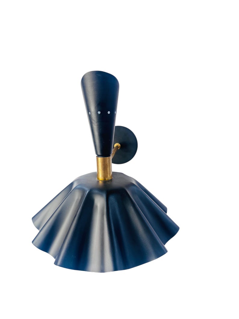 Op de afbeelding: Een marineblauwe wandlamp met een uniek ontwerp. De lamp heeft een uitlopende, gerimpelde kap en een conische bovenkant met drie kleine witte stippen. De basis is goudkleurig en de armatuur is gemonteerd op een cirkelvormige zwarte plaat.