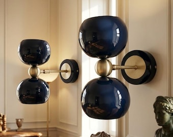 May include: Two wall-mounted light fixtures featuring a brass arm and a circular black base. Each fixture consists of two stacked, glossy dark blue spherical glass shades separated by a central brass sphere, creating a vertical hourglass shape.