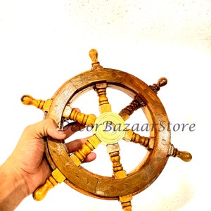May include: A wooden ship's wheel with a brass center hub and six spokes. The wheel is brown and has a natural wood finish. The wheel is approximately 12 inches in diameter.