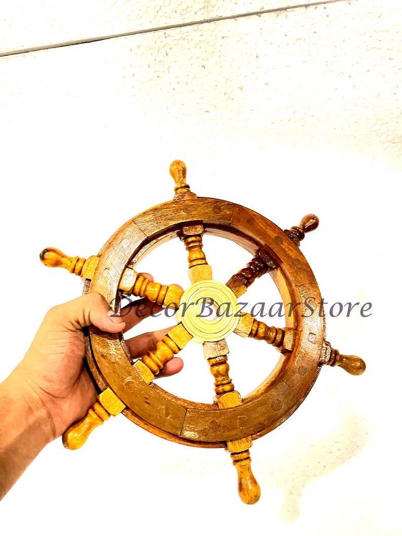 May include: A wooden ship's wheel with a brass center hub and six spokes. The wheel is brown and has a natural wood finish. The wheel is approximately 12 inches in diameter.