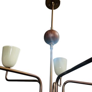 Puede incluir: Un candelabro moderno de mediados de siglo con acabado de lat&oacute;n y pantallas de vidrio blanco. El accesorio tiene un v&aacute;stago central con una esfera de madera y un dosel circular. Los brazos se extienden hacia afuera, sosteniendo las pantallas hacia arriba.