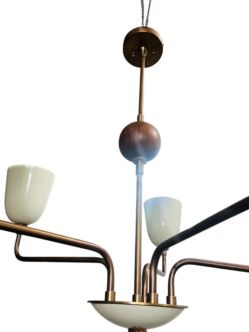 Puede incluir: Un candelabro moderno de mediados de siglo con acabado de lat&oacute;n y pantallas de vidrio blanco. El accesorio tiene un v&aacute;stago central con una esfera de madera y un dosel circular. Los brazos se extienden hacia afuera, sosteniendo las pantallas hacia arriba.