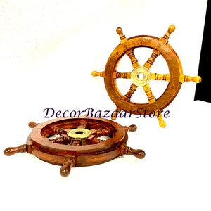 May include: Two wooden ship steering wheels with brass accents. The wheels are brown with a light brown wood grain. The wheels have six spokes and a brass center hub. The wheels are on a white background.