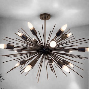May include: A modern, sputnik-style chandelier with multiple light bulbs. The fixture has a dark bronze finish and radiating arms, creating a starburst effect. The bulbs are elongated and emit a warm, inviting glow, perfect for a living room or dining area.