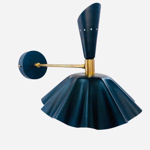 Op de afbeelding: Een donkerblauwe wandlamp met een messing arm en accenten. De lamp heeft een uitlopende kap en een conische bovenkant met drie kleine witte stippen. De lamp is ontworpen om aan de muur te worden bevestigd.