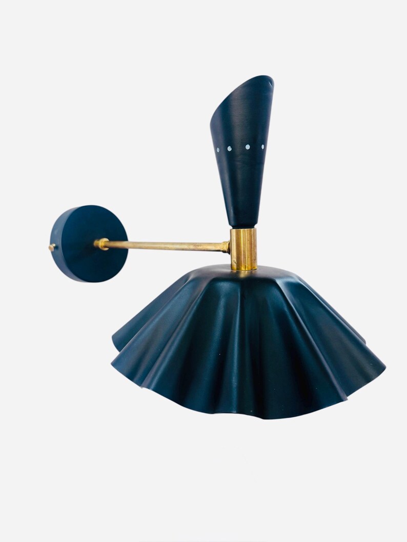 Op de afbeelding: Een donkerblauwe wandlamp met een messing arm en accenten. De lamp heeft een uitlopende kap en een conische bovenkant met drie kleine witte stippen. De lamp is ontworpen om aan de muur te worden bevestigd.