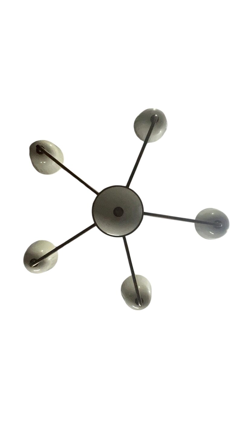 Puede incluir: Una l&aacute;mpara de ara&ntilde;a moderna con un elemento central circular y seis brazos que se extienden hacia afuera. Cada brazo tiene una peque&ntilde;a pantalla de vidrio blanco roto redondeada. Los brazos y el elemento central son de metal oscuro, creando un dise&ntilde;o de estrella.