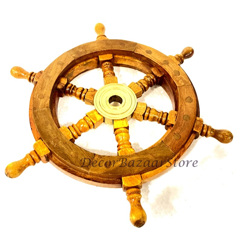 May include: A wooden ship's wheel with a brass center hub and six spokes. The wheel has a diameter of approximately 15 inches and is made of dark brown wood. The spokes are decorated with a carved design. The wheel is a decorative item and is not intended for use on a boat.