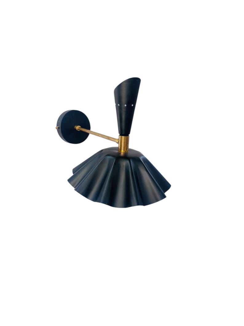 Op de afbeelding: Een moderne wandlamp met een donkerblauwe, geplooide kap en een arm in messingkleur. De lamp heeft een zwarte, kegelvormige bovenkant en een ronde wandbevestiging. Het ontwerp is strak en stijlvol, geschikt voor binnenverlichting.