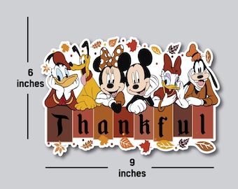 May include: A Thanksgiving-themed sticker featuring Mickey Mouse, Minnie Mouse, Donald Duck, Goofy, and Pluto. The characters are smiling and standing in front of a wooden fence with the word "Thankful" written on it. The sticker is decorated with autumn leaves.