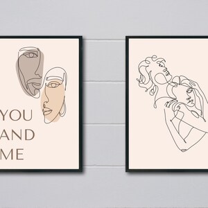 以下が含まれることがあります： ベージュの背景に、ミニマルな線画のプリントが2つあります。最初のプリントは、2つの顔と「YOU AND ME」というテキストが描かれています。2つ目のプリントは、抱き合っている2つの図形が描かれています。