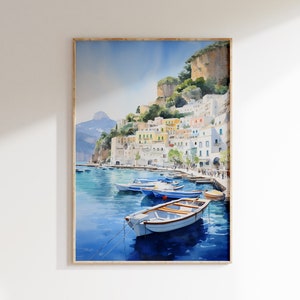 May include: Watercolor painting of a colorful Italian village on a cliffside overlooking a blue bay with several small boats docked. The painting is framed in a light wood frame.