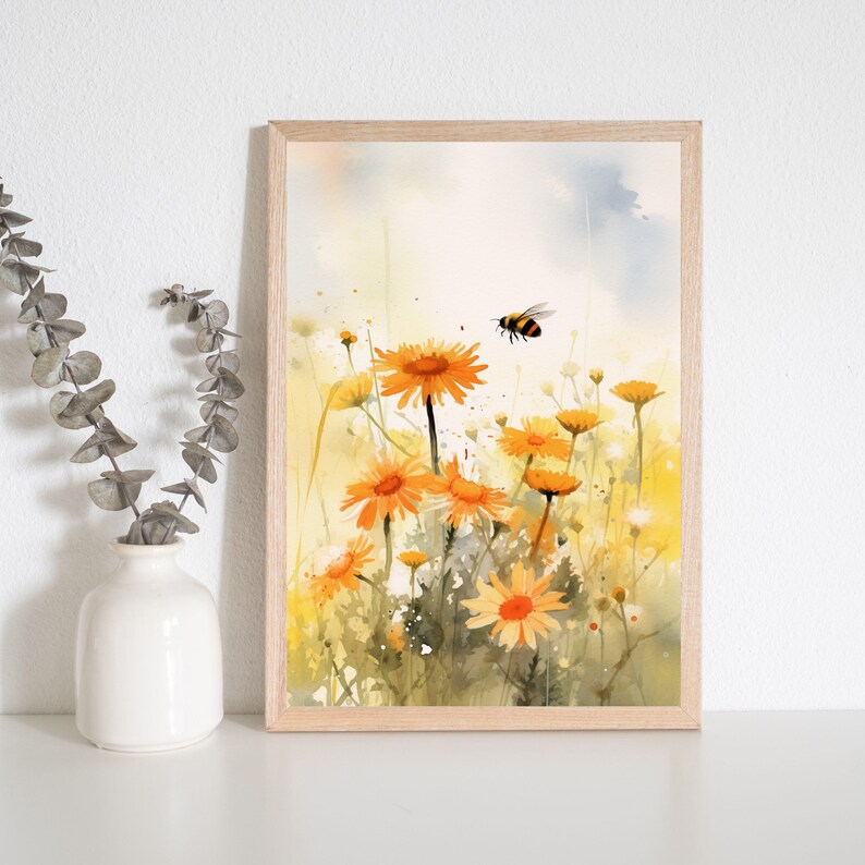 May include: Watercolor print of orange daisies in a field with a flying bee. The artwork is framed in a light wood frame. The background is a soft blend of yellow and blue hues, creating a serene and natural scene.