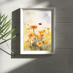 May include: A framed watercolor print featuring a field of orange daisies with a flying bee. The artwork has a soft, painterly style with yellow and green hues. The white frame sits on a light wood surface, with a green leaf in the corner.