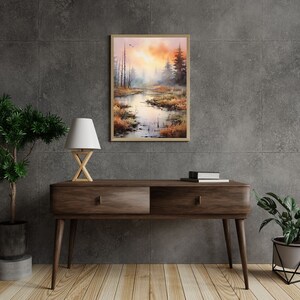 May include: A watercolor painting of a misty forest scene with a river flowing through it. The painting is framed in a light wood frame and hangs on a gray wall.