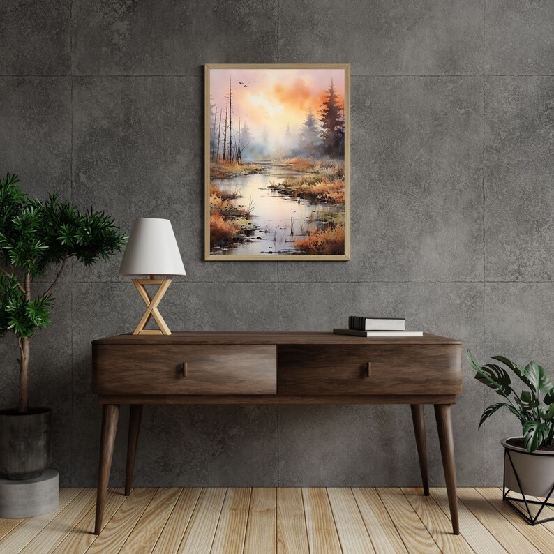 May include: A watercolor painting of a misty forest scene with a river flowing through it. The painting is framed in a light wood frame and hangs on a gray wall.