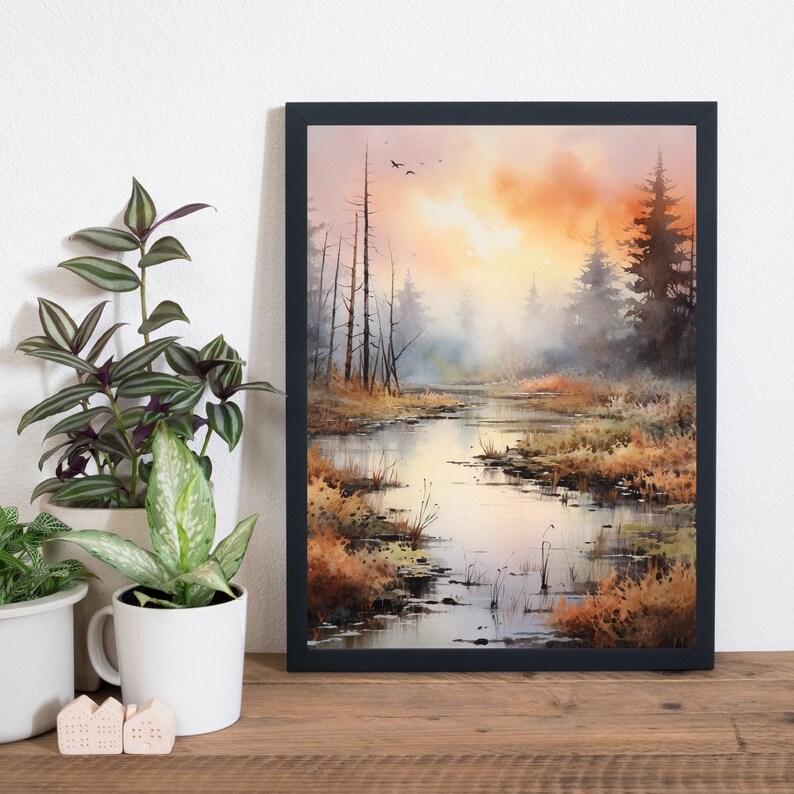 May include: A framed watercolor painting depicting a misty forest scene with a winding river in the foreground. The sky is a soft orange and pink, with a few birds flying overhead. The trees are silhouetted against the sky, and the water is a reflective blue.
