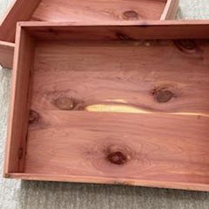 May include: Two open, rectangular cedar wood boxes. The boxes are a reddish-brown color with visible wood grain and knots. The boxes are empty and appear to be new.
