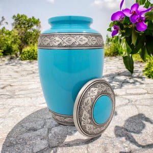 May include: A blue and silver cremation urn with a decorative floral pattern. The urn has a lid with a matching design.