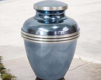 May include: A blue metal cremation urn with a silver lid and trim. The urn has a smooth, polished finish.