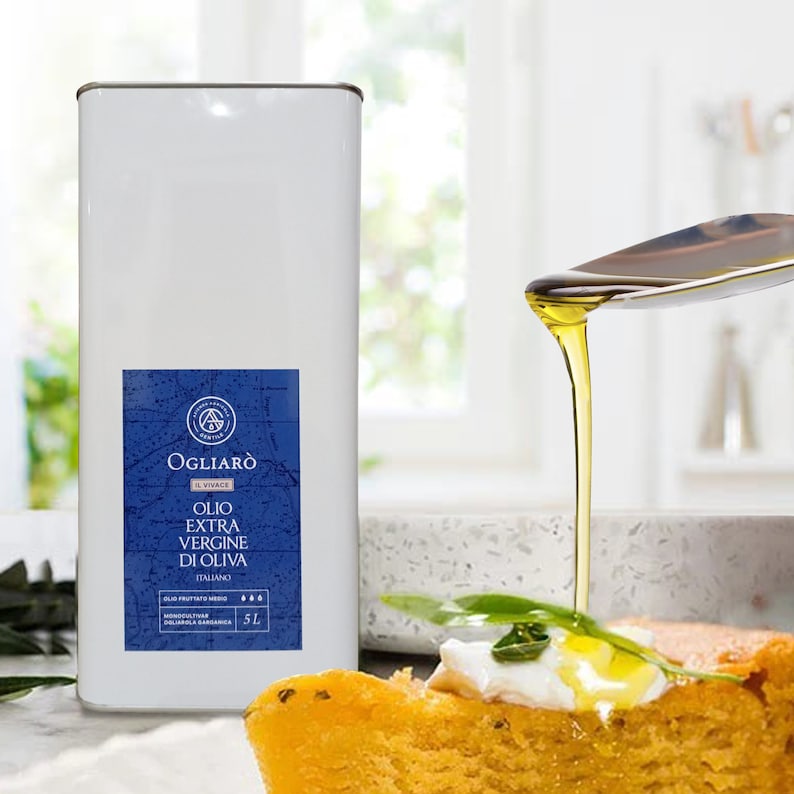 May include: A white tin can with a blue label that says "OGLIAR&Ograve; IL VIVACE OLIO EXTRA VERGINE DI OLIVA ITALIANO" and a picture of a compass. The can is 5 liters and is sitting on a white countertop. A spoon is pouring olive oil onto a slice of bread with a white topping.