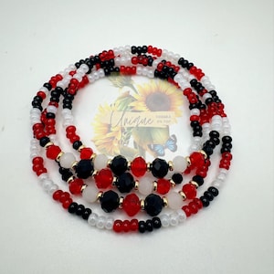 May include: A multi-strand waist bead necklace with red, white, and black beads. The beads are arranged in a repeating pattern. The necklace is made with small seed beads and larger, faceted beads.