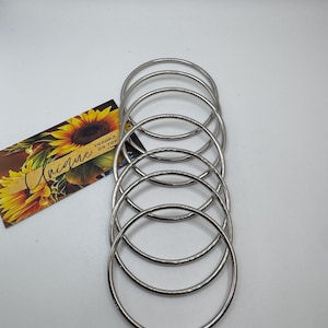 May include: A set of six silver bangle bracelets. The bracelets are stacked on top of each other.