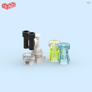 May include: A selection of small building blocks in various colours. The set includes a white base with a black double-barrel piece, a clear circular piece, and two transparent tower-shaped pieces in yellow and blue. The Stud Factory logo is in the top left corner.