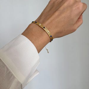 May include: A gold bracelet with a textured surface and blue and white beads.