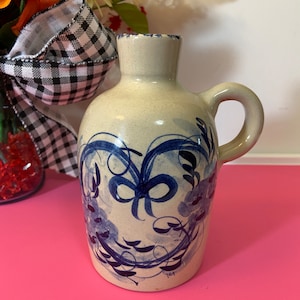 May include: A beige ceramic jug with a handle and a narrow neck. The jug is decorated with blue floral designs. The jug has a small handle on the side. The jug is likely used for decorative purposes.
