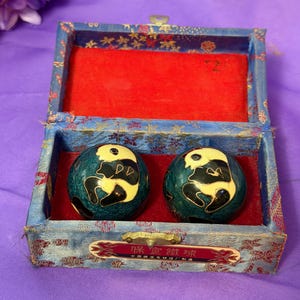 May include: Two spherical metal meditation balls with a dark teal finish and a black and cream panda bear design, housed in a rectangular blue fabric-covered box with a red velvet interior and a metal latch featuring Chinese characters.