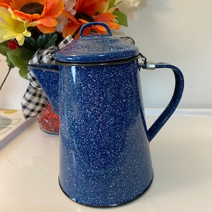May include: Blue enamel coffee pot with white speckles and a black rim. The pot has a lid with a handle and a spout.