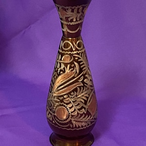 May include: A decorative vase with a flared gold rim and base. The vase has a dark red body with intricate gold and copper-colored floral patterns. The vase is approximately 8 inches tall.
