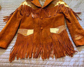 Puede incluir: Chaqueta de ante marrón con largos flecos en las mangas, el pecho y los bolsillos. La chaqueta tiene cuello y cierre de botones. Parches de piel de vaca blanca y marrón en los hombros y bolsillos. Prenda de estilo western vintage.