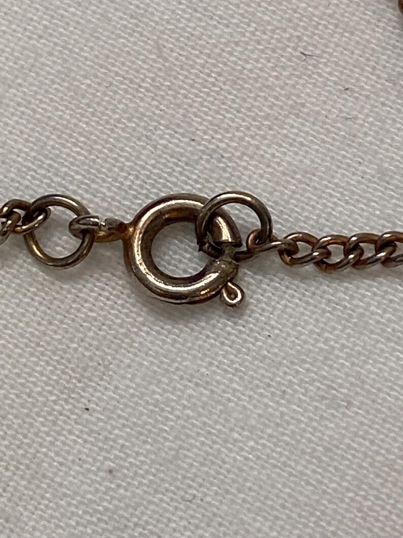 May include: Close-up of a gold-colored necklace clasp and chain. The clasp is a circular spring ring type, and the chain links are small and oval. The background is a light-colored fabric.